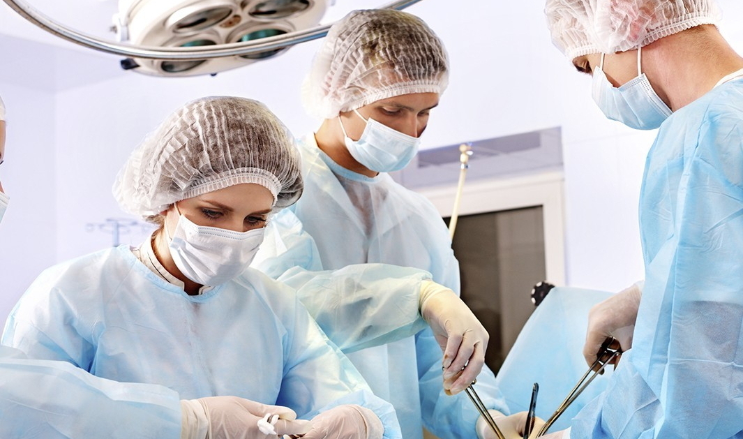 Хирурги в медицинских халатах и шапочках проводят операцию